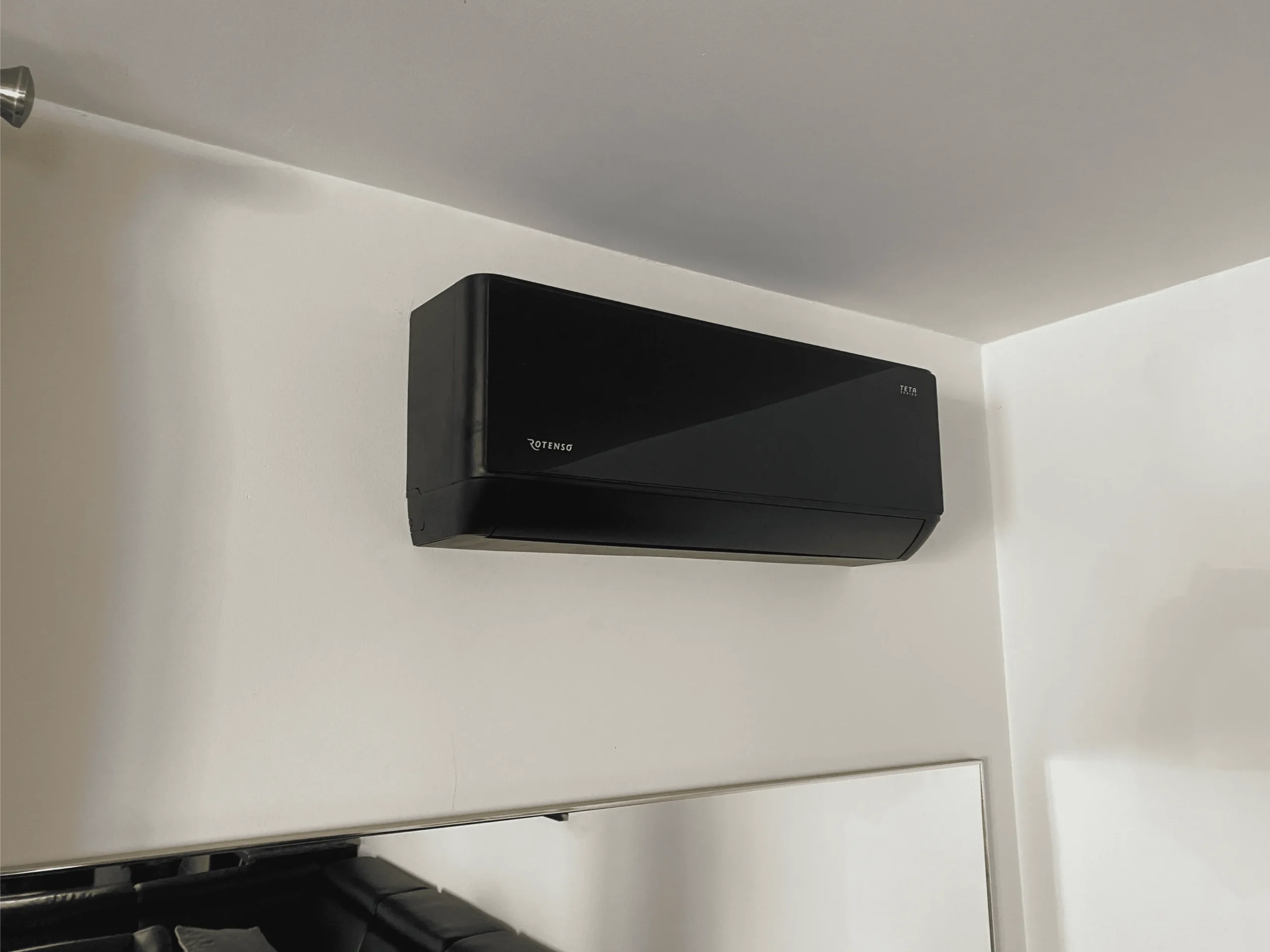 Czarna jednostka wewnętrzna klimatyzacji zamontowana na białej ścianie nad lustrem Klimatyzacja