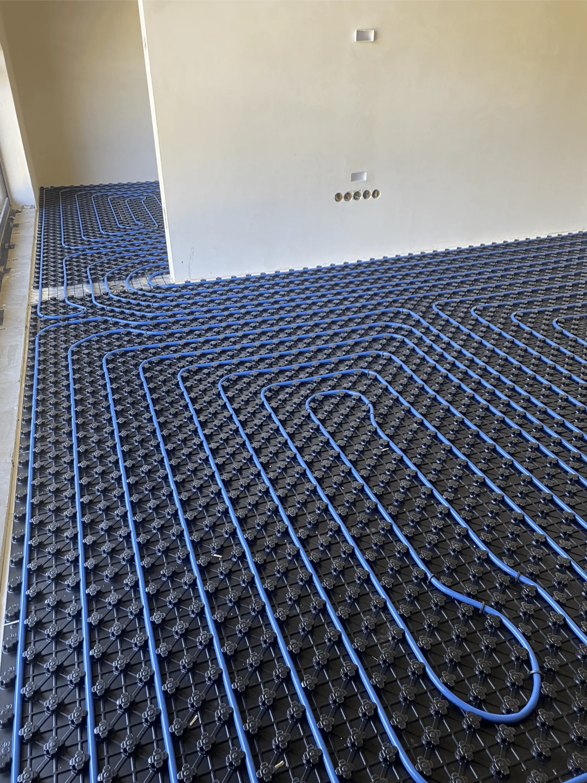 Ogrzewanie podłogowe – niebieskie rury ułożone w pętle na czarnych matach izolacyjnych