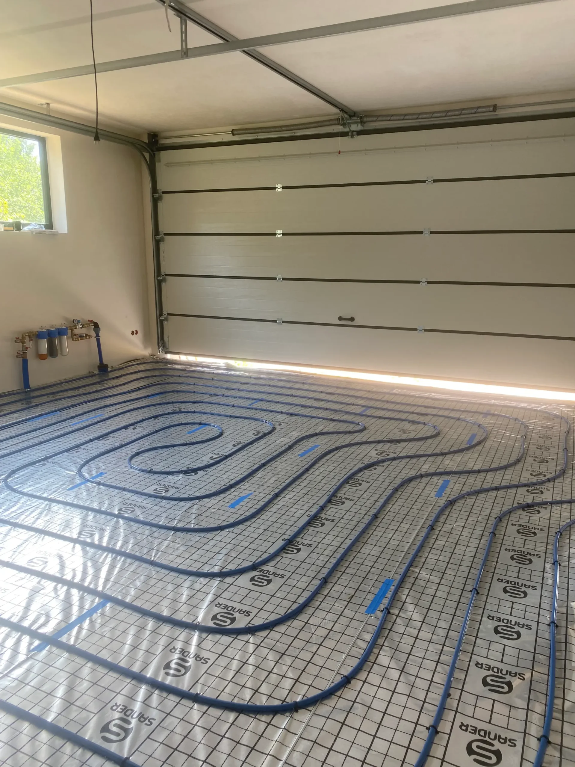 Ogrzewanie podłogowe w garażu – widoczne błękitne rury ułożone na refleksyjnej folii i siatce