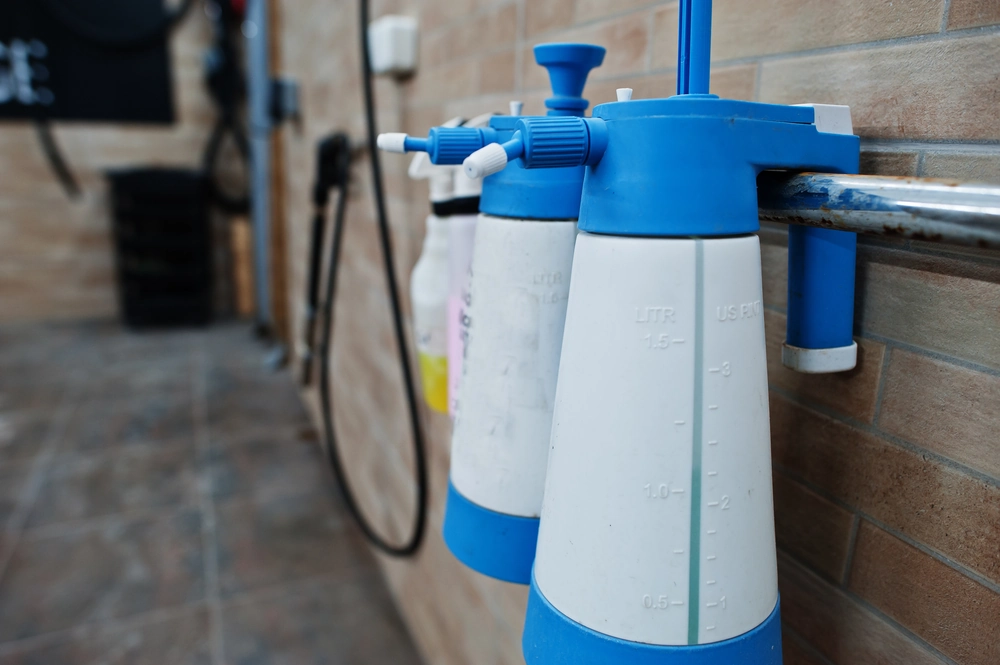 Trzy plastikowe opryskiwacze ścienne z niebieskimi elementami i miarką objętości