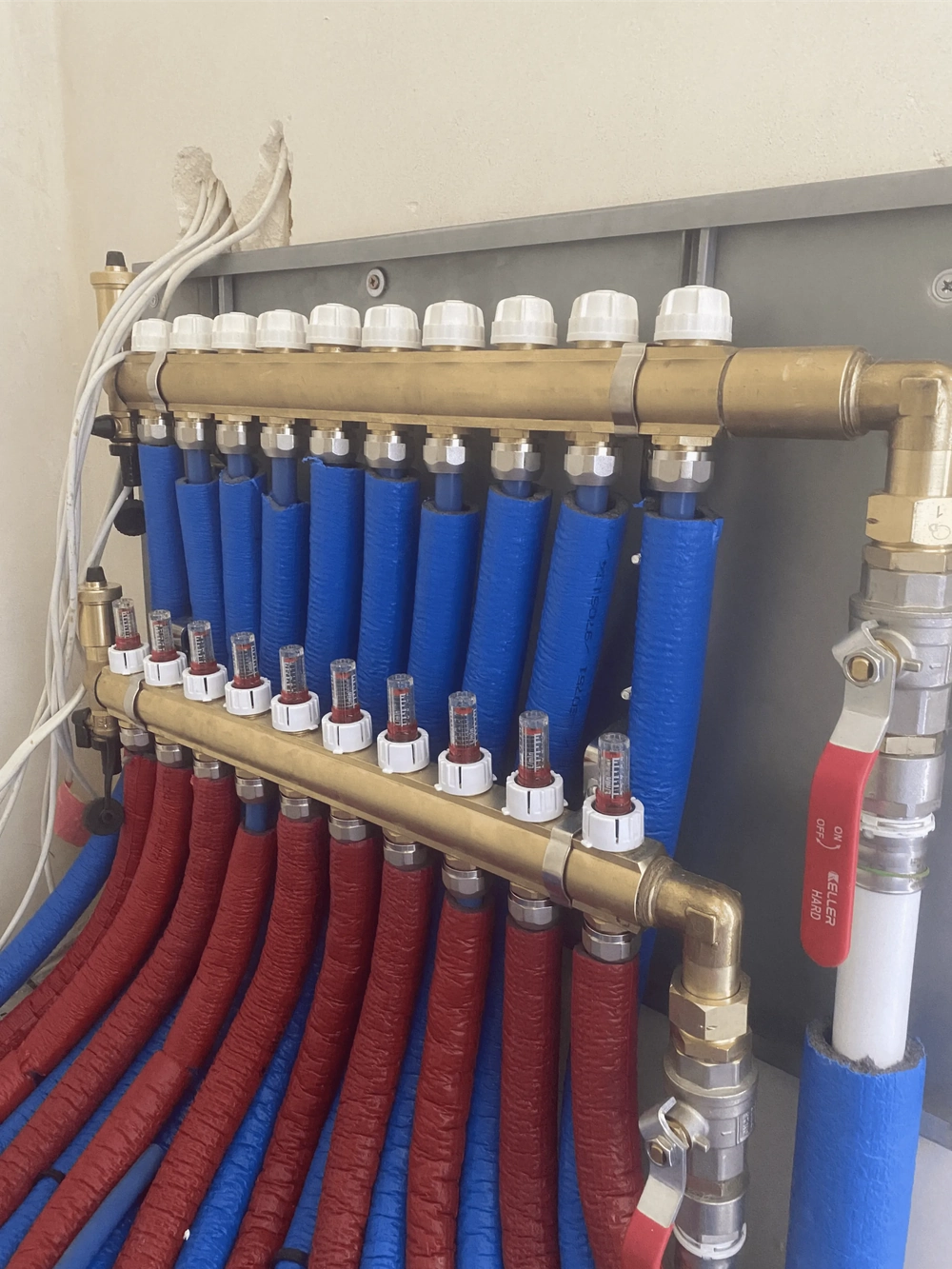 Rozdzielacz ogrzewania podłogowego z mosiężnym kolektorem, przepływomierzami i izolowanymi rurami czerwonymi i niebieskimi